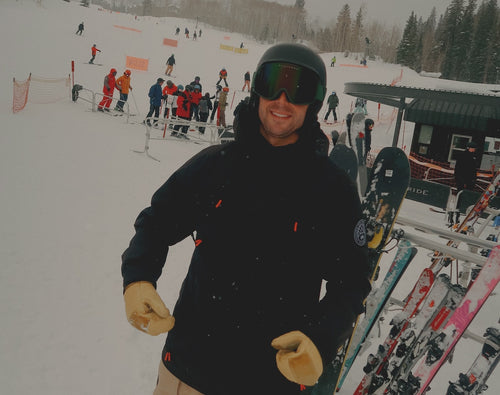 A person in ski gear smiles on a snowy slope, with skis and people in the background.