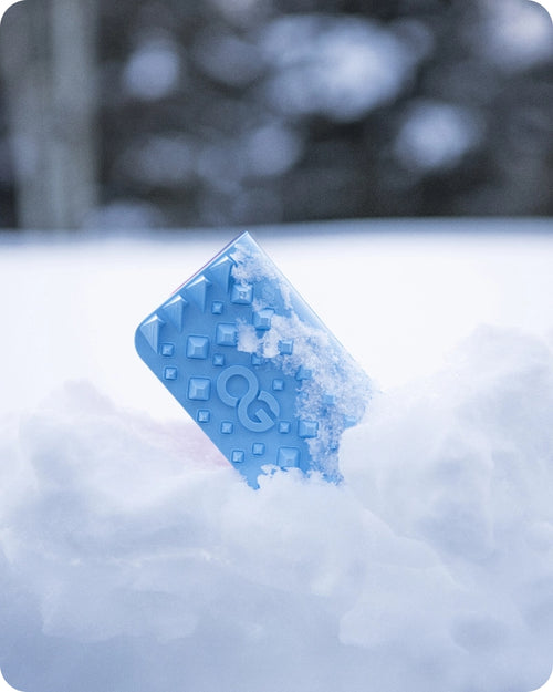 A blue smartphone partially buried in the snow, featuring embossed patterns and a logo on the back.