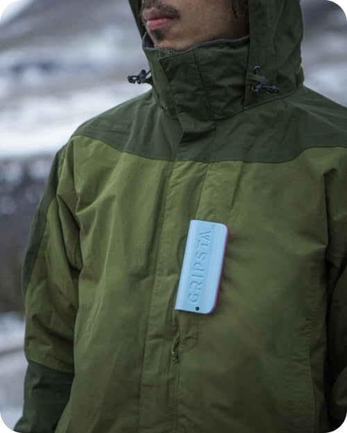 Person in a green jacket with a phone in the chest pocket, standing outdoors.